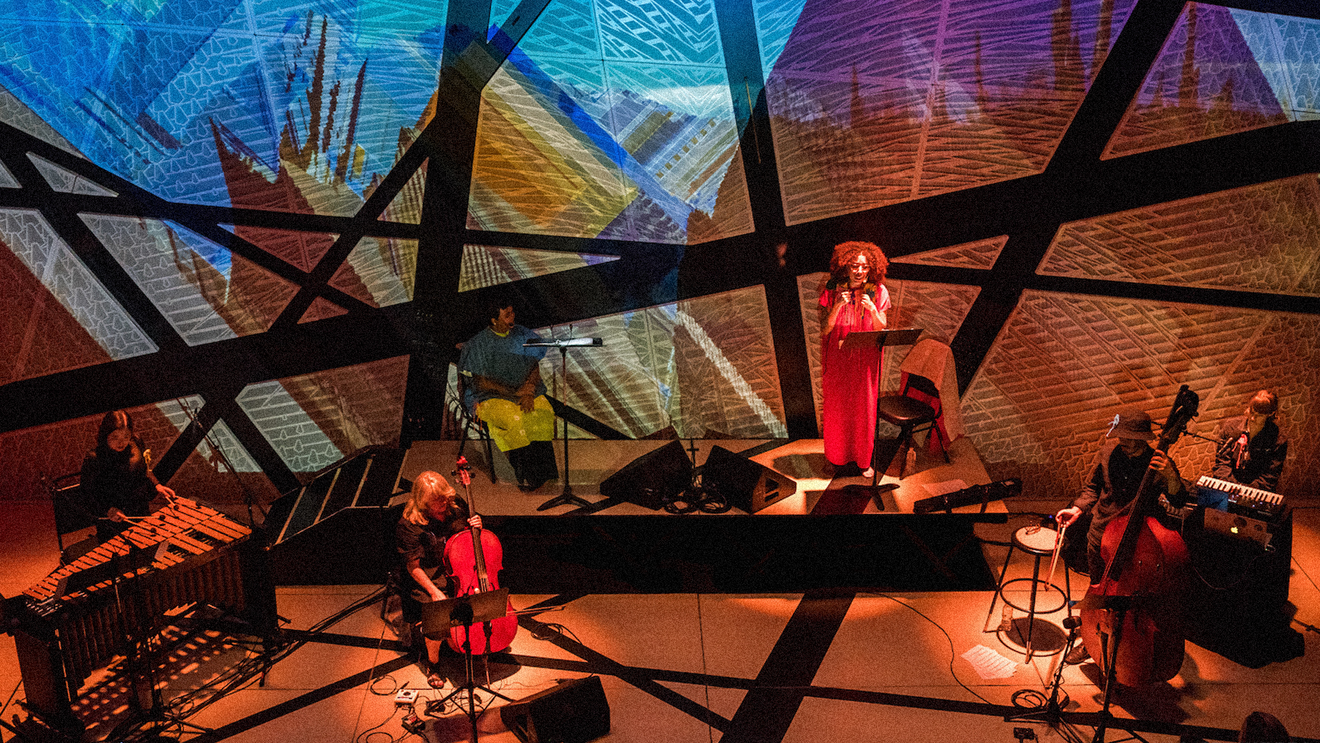 Musicians performing inside a colorful projection environment.